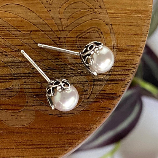 Pearl earrings on a wooden surface with a plant in the background