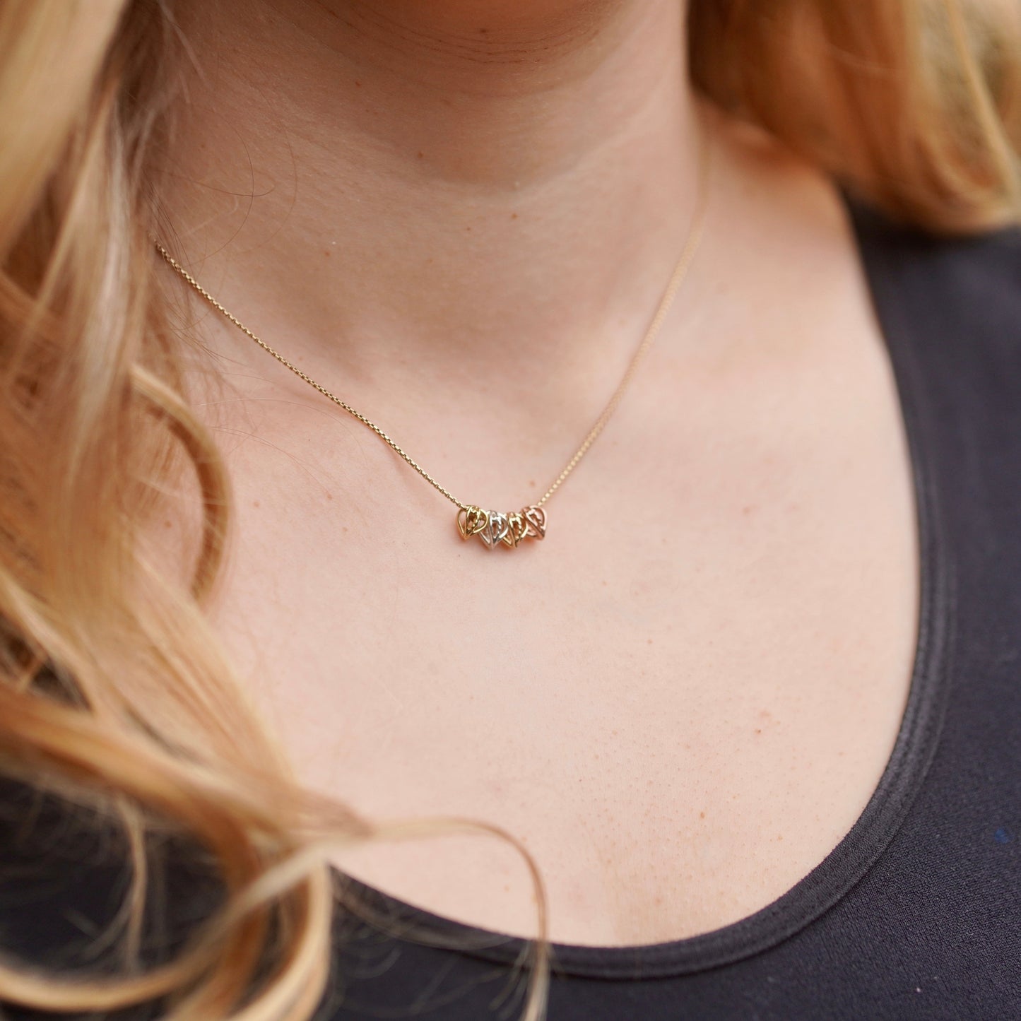 Close-up of a gold necklace worn by a person with blonde hair.