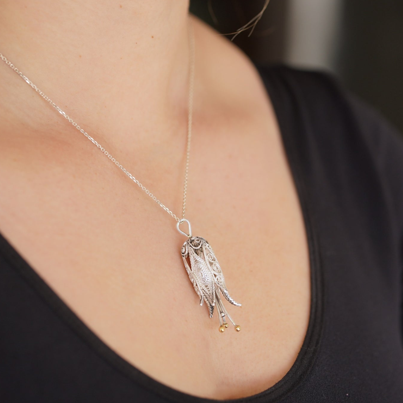 Silver necklace with a pendant worn by a person against a neutral background