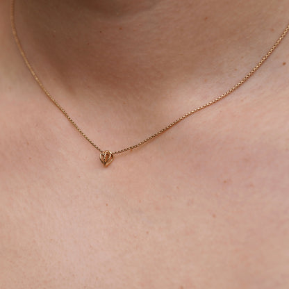 Gold necklace with a leaf pendant on a person's neck