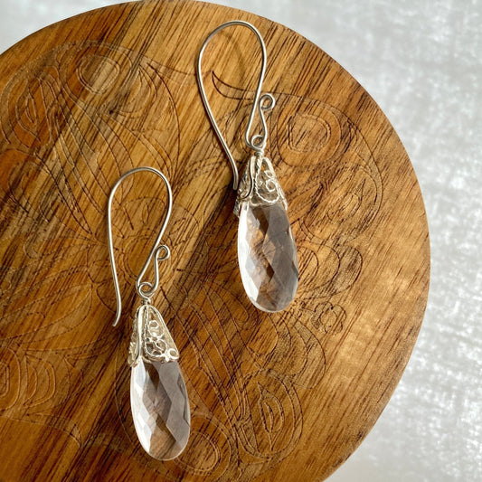Silver earrings with teardrop-shaped stones on a wooden surface