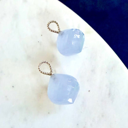Two light blue faceted gemstone drops with twisted silver wire loops, displayed on a white marble surface