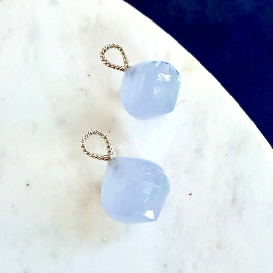 Two light blue faceted gemstone drops with twisted silver wire loops, displayed on a white marble surface
