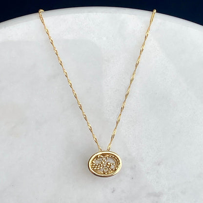 A delicate gold chain necklace with the back of an oval pendant featuring an intricate filigree design, displayed on a white marble surface against a dark navy background.