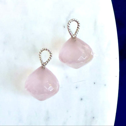 A pair of rose quartz drops with twisted silver wire loops, displayed on a white marble surface with a dark blue background visible on the right.